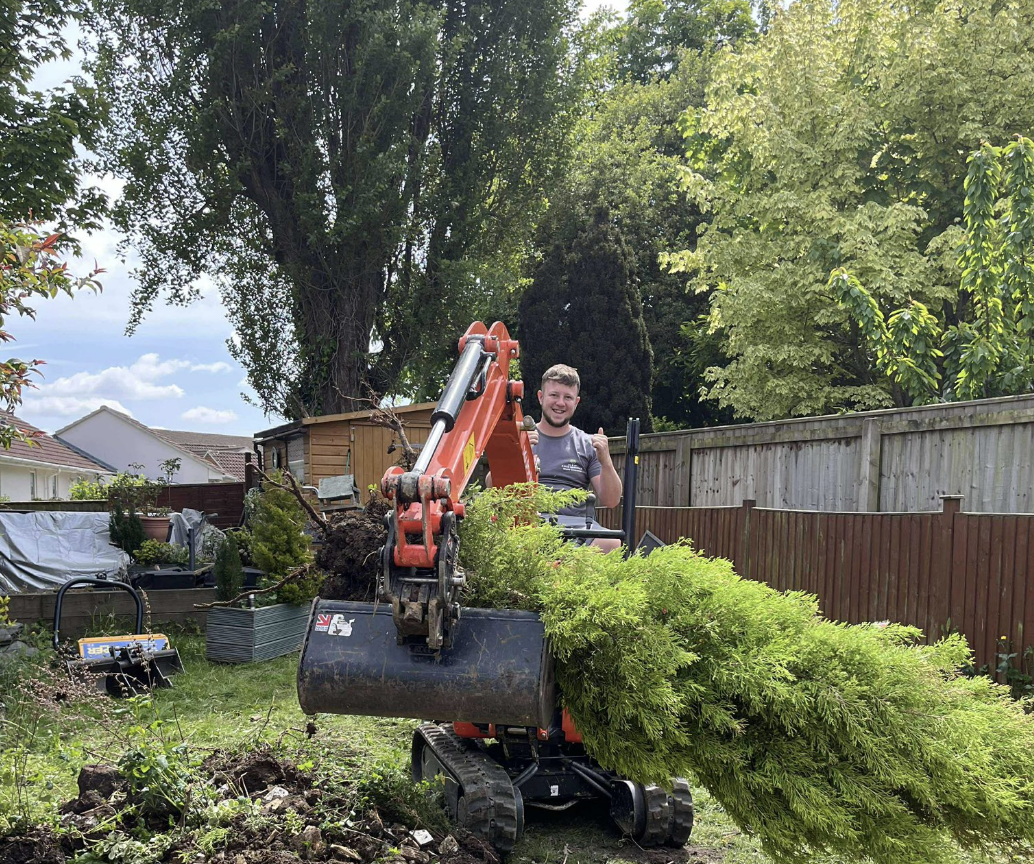 CJLEE Landscapes team member operating excavator in residential garden with large conifer, demonstrating professional landscaping services